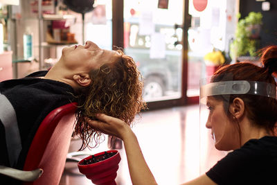 Hairdresser with a face shield dries her client's hair in her salon