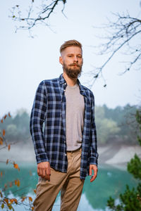 Young caucasian bearded man in plaid shirt traveling alone in autumn forest