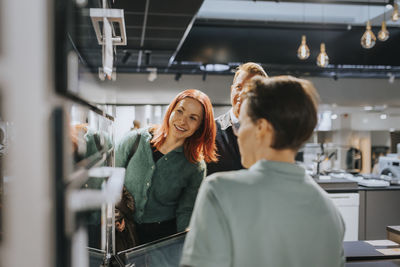 Happy couple looking at microwave oven while saleswoman assisting at electronics store