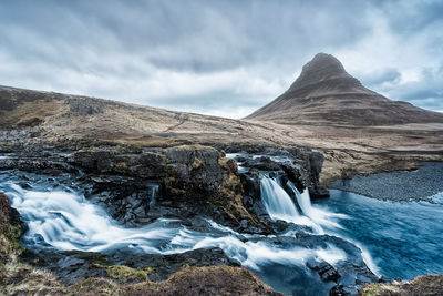 Scenic view of waterfall against cloudy sky