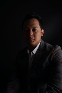 Portrait of young businessman against black background