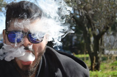 Close-up of man wearing sunglasses blowing smoke outdoors