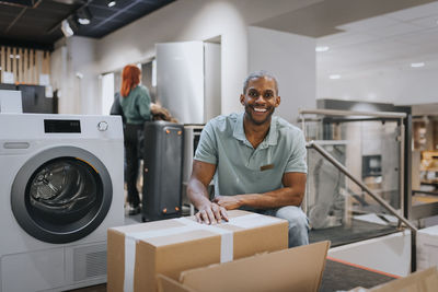 Portrait of smiling mature salesman with cardboard box in appliances store