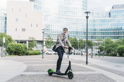 Businessman with electric push scooter standing in front of modern office buildings
