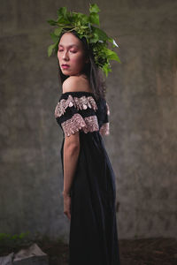 Young woman looking away while standing against wall