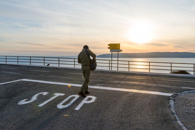 Rear view of man on road by sea during sunset