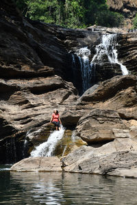 Woman sitting on rock at waterfall