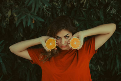 Close-up of woman holding orange against tree