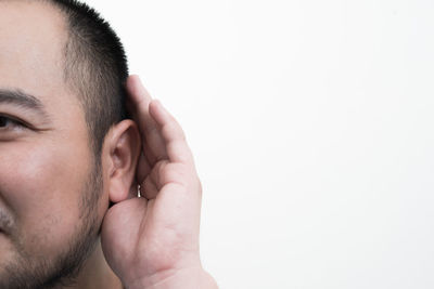 Close-up of mid adult man with hand covering ear against white background