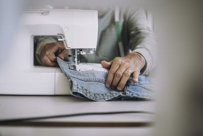 Midsection of male design professional working on sewing machine at workshop