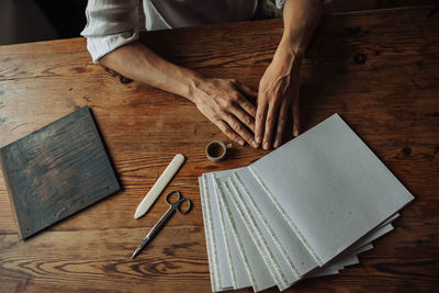 Hands of artist, paper sheets, scissors on a wooden table, top view