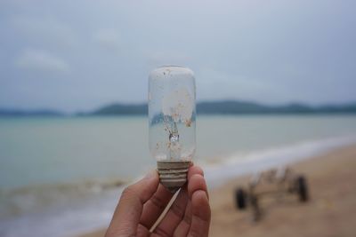 Close-up of hand holding glass of water at beach against sky