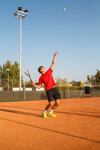 Man playing tennis on court against clear blue sky
