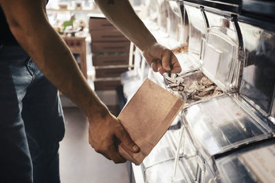 Midsection of male customer filling slice coconut in paper bag at organic store