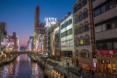 Canal amidst illuminated buildings in city during sunset