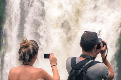 Rear view of friends photographing waterfall
