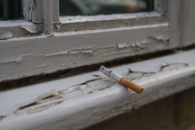 Close-up of burning cigarette on weathered window sill