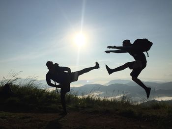 Silhouette man with arms raised on field against sky