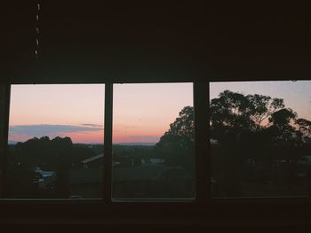 Silhouette landscape against sky seen through window