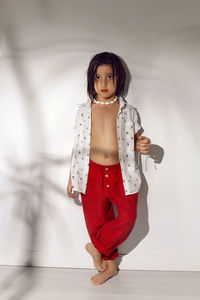 Portrait of a hawaiian boy child in red pants stand next to a white wall and a palm tree