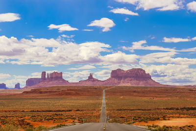 Empty road leading towards rock formations against sky