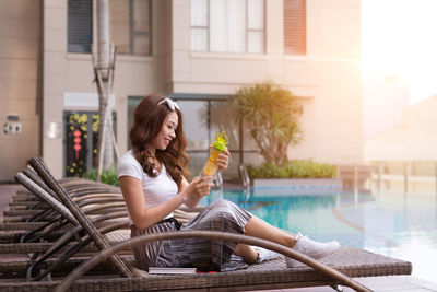 Woman sitting on chair by swimming pool