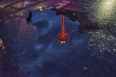 Reflection of tower in puddle on street at night