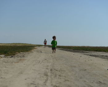 Full length of little boy running on the beach and woman standing behind him on field