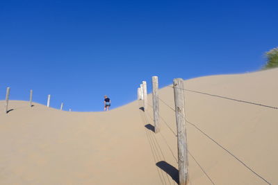 Low angle view of people on sand dune against clear blue sky