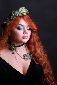 Sensuous young woman wearing wreath and necklace against black background