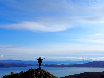 Man standing on rock by sea against sky