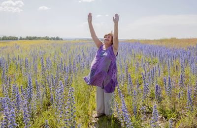 Woman standing on field by purple flowering plants against sky