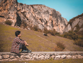 Man sitting on rock against mountains