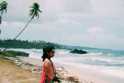 Side view of thoughtful woman with camera standing at beach