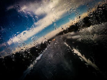 Full frame shot of wet glass window against cloudy sky