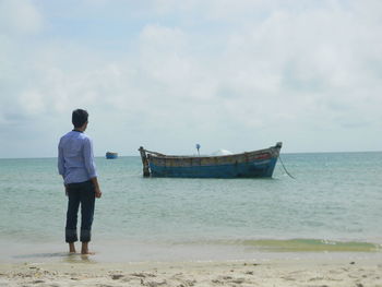 Rear view of man standing on beach against sky