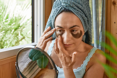 Portrait of young woman looking through window at home