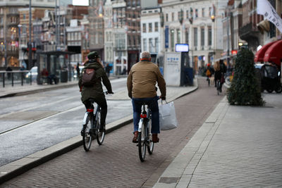 Rear view of people riding bicycle on city street