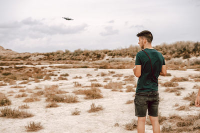 Rear view of young man flying drone on field