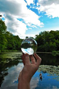 Close-up of hand holding crystal ball with reflection of trees, lake and sky in dulwich park, london