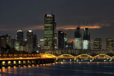 Illuminated city by river against sky at night