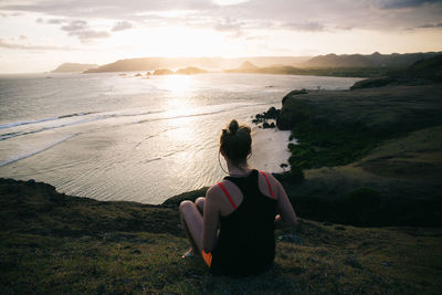 Rear view of woman sitting on beach at sunset