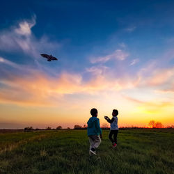 Boys on field against sky during sunset