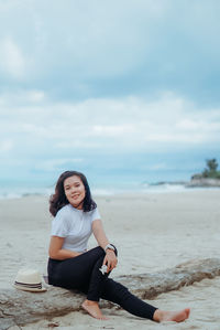 Young woman sitting at beach against sky