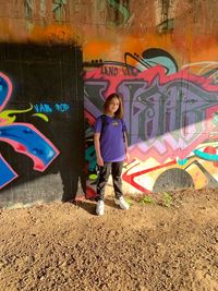 Full length of girl standing against graffiti wall