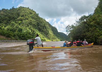 People sitting on riverbank against sky