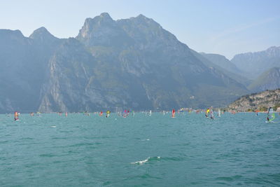 People on sea by mountains against sky