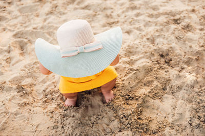 High angle view of baby wearing hat crouching on sand