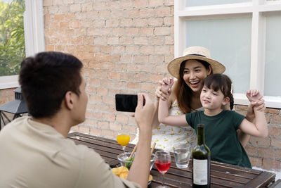 Father clicking picture of smiling mother and daughter outdoors