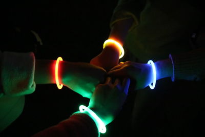 Cropped hands of friends wearing illuminated rubber bracelets at night